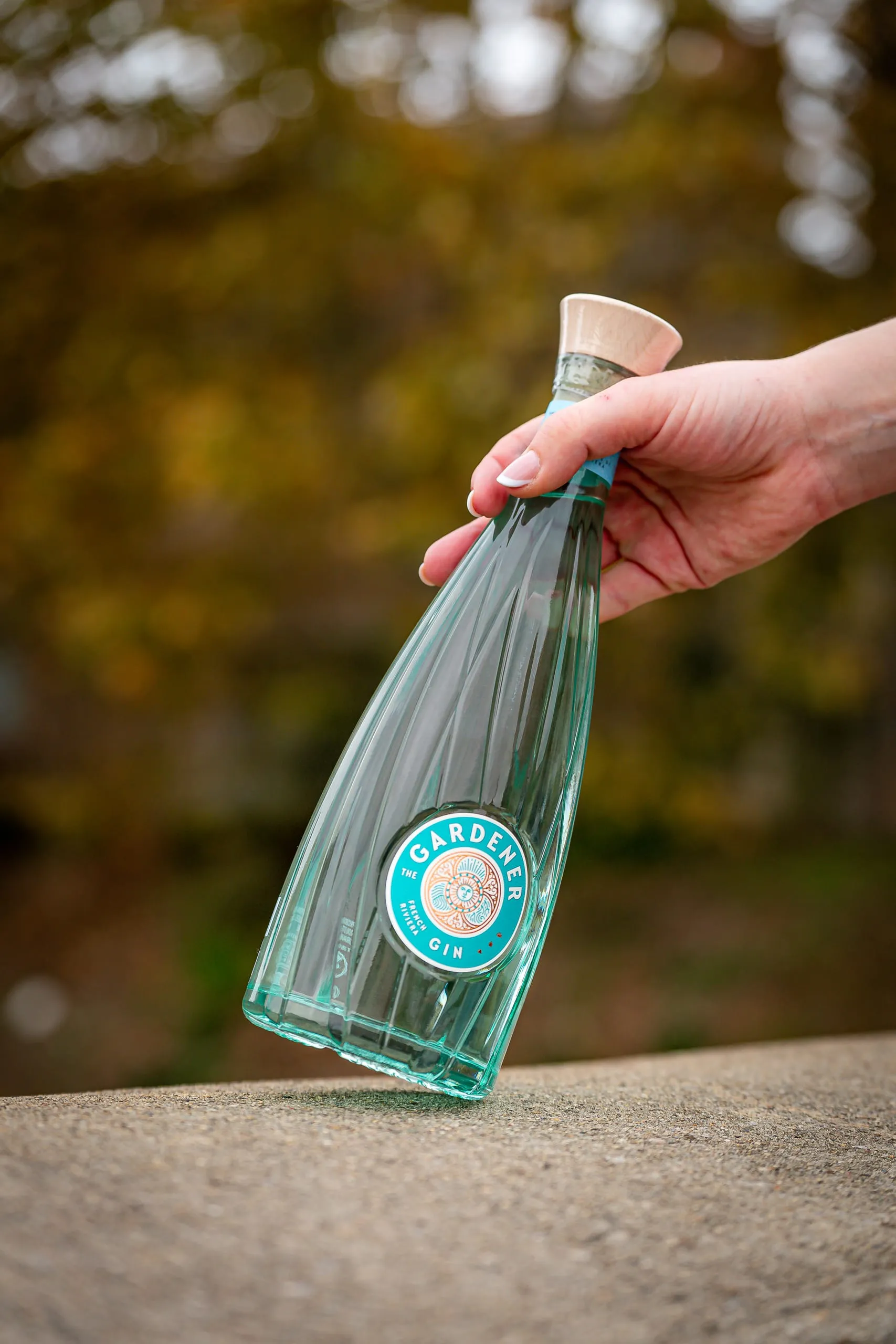 Main tenant une bouteille transparente de gin devant un arrière-plan végétal